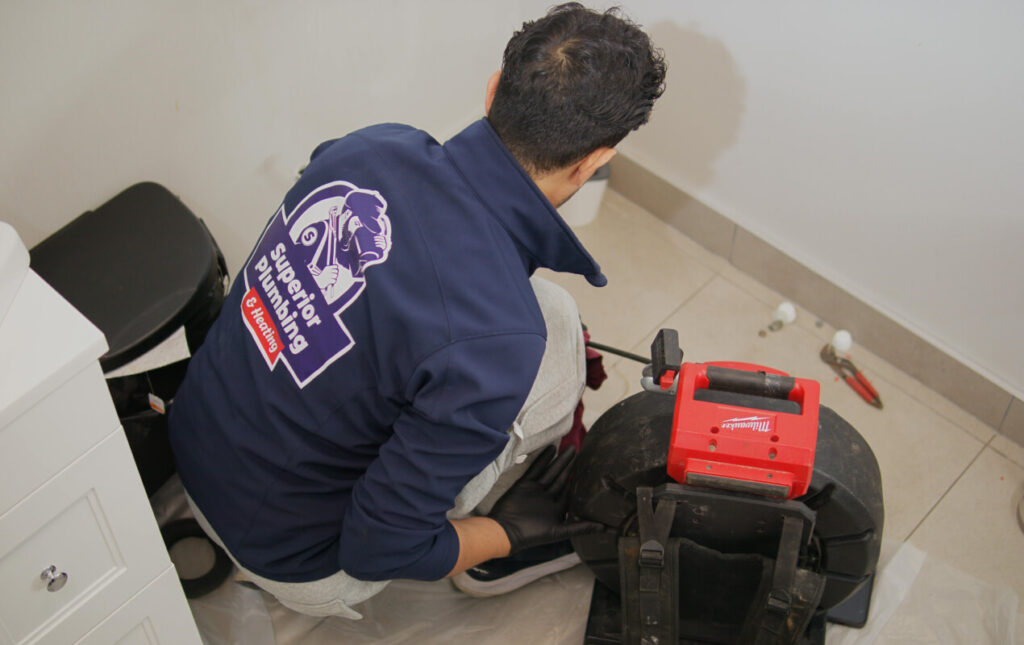 Superior Plumbing & Heating technician performing Drain Snaking using a professional Milwaukee machine to clear a drain
