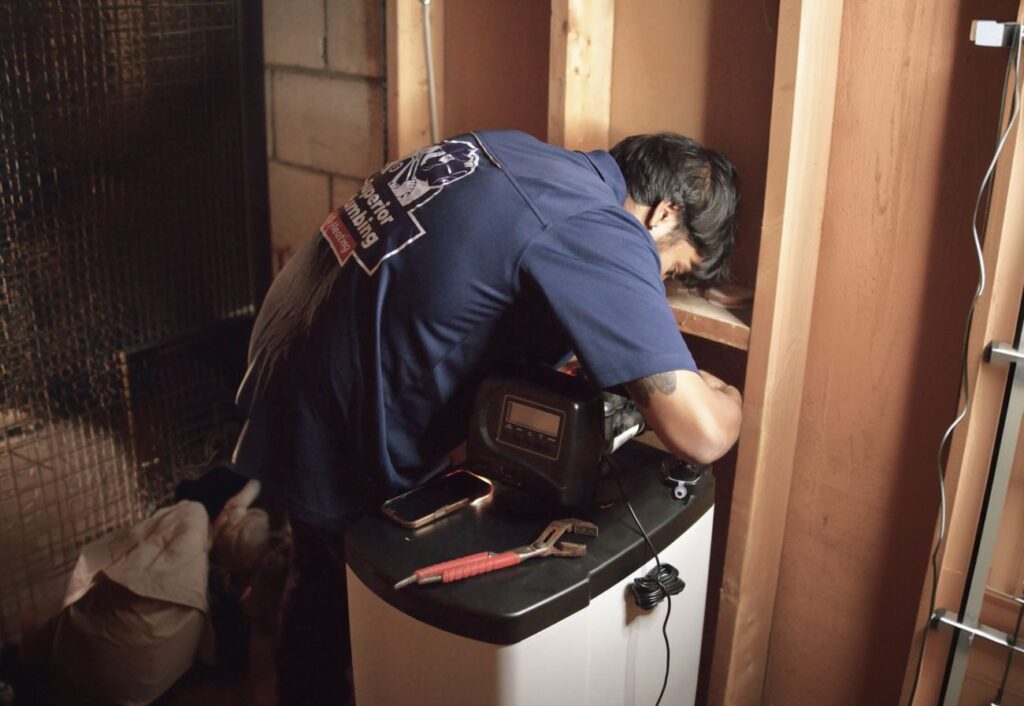 Superior Plumbing & Heating expert Water Softener Repair being performed on a white cabinet-style unit by a skilled technician