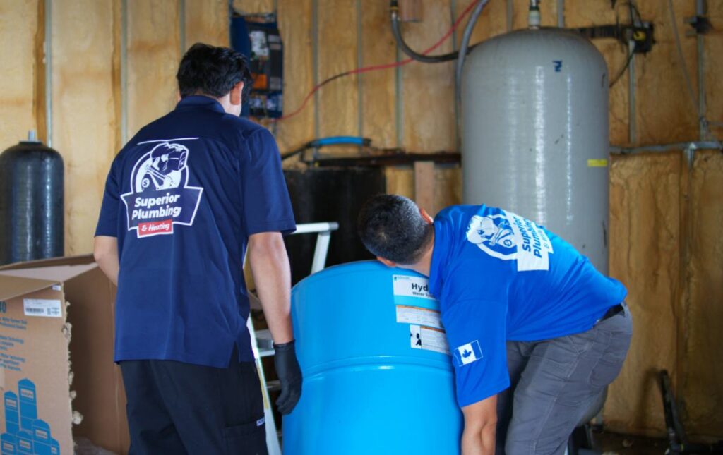 Two professionals from Superior Plumbing & Heating positioning a blue pressure tank for a well pump installation local
