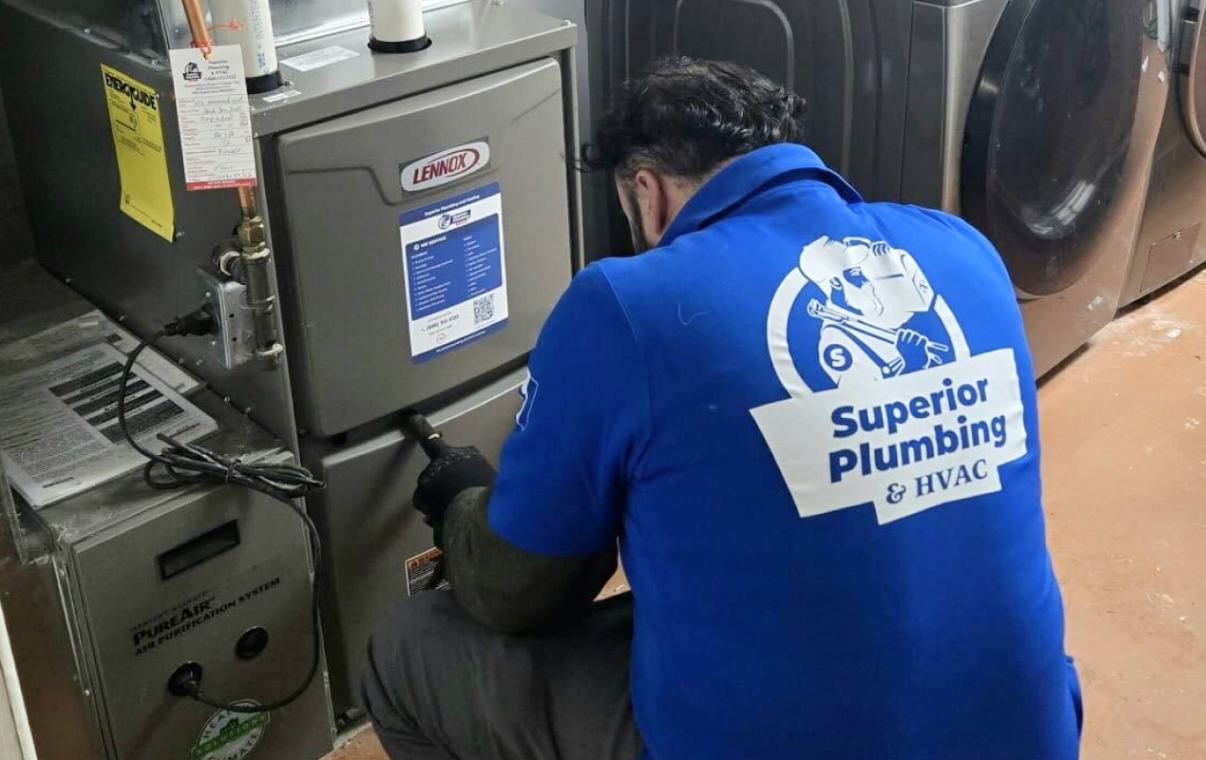 Technician kneeling to service a Lennox gas furnace in a basement laundry room during a fall tune-up